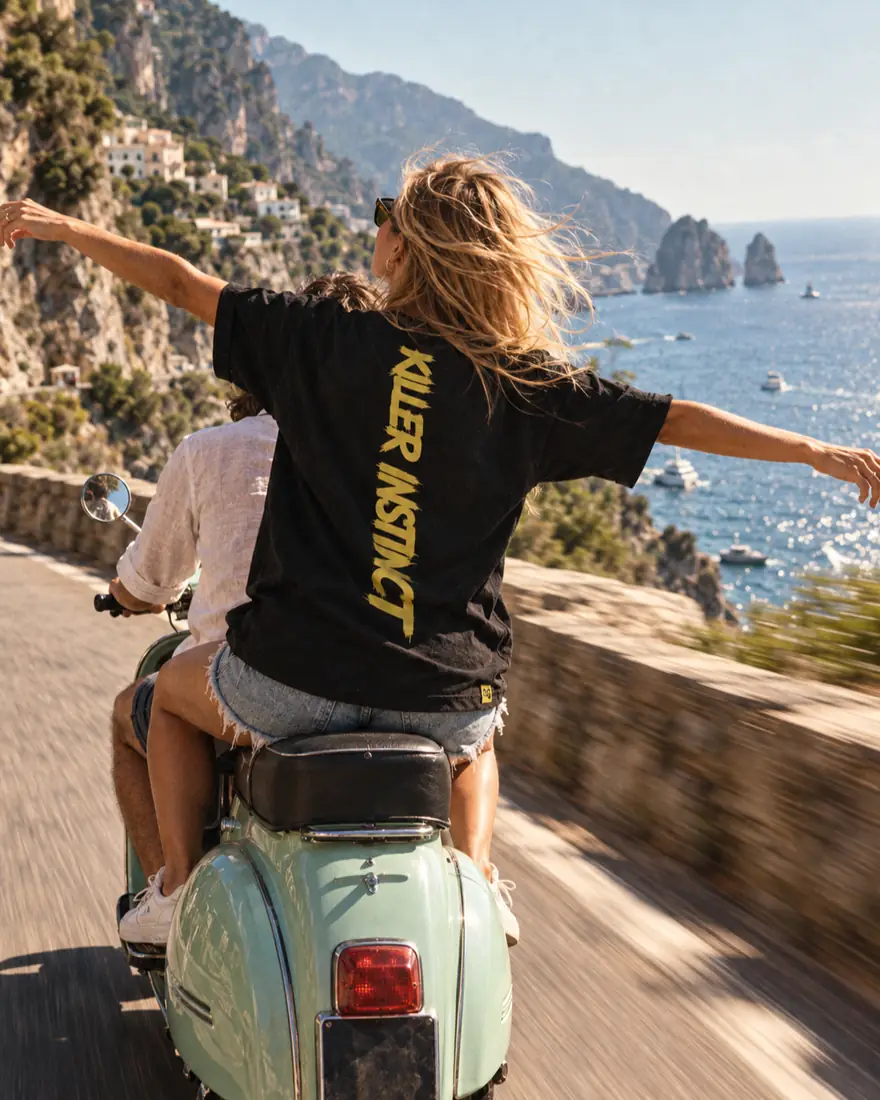 Ragazza in Vespa sulla costa, di spalle, con la maglia nera Killer Instinct
